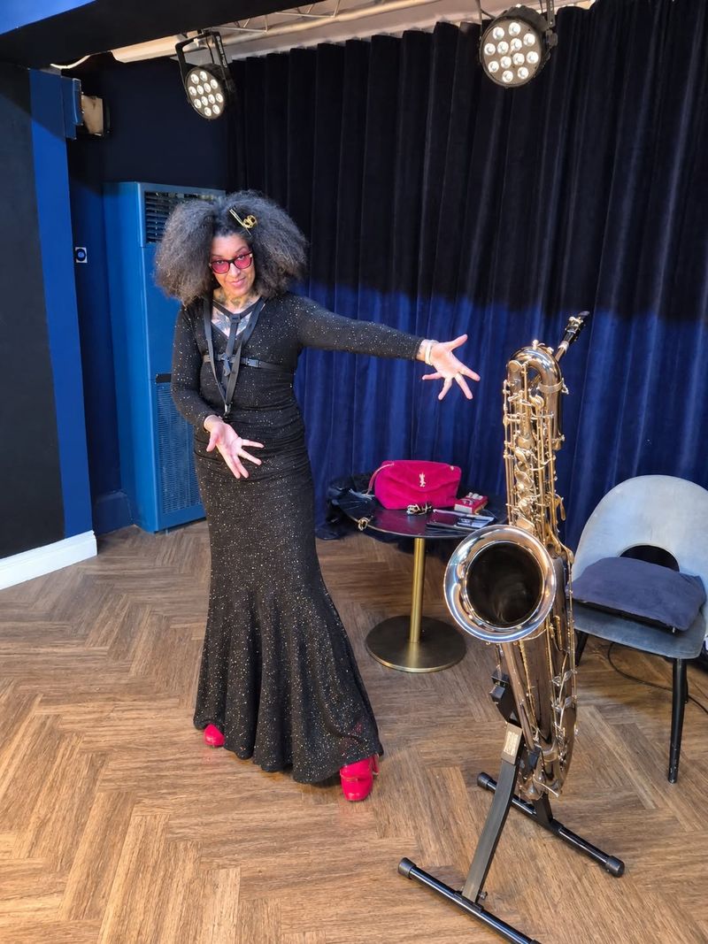 Rosemary Quaye in a black sequinned gown and red heels presenting her saxophone on its stand at an event venue